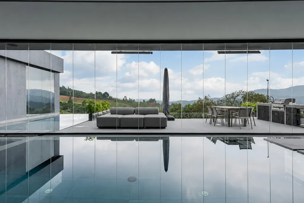 Cerramiento FlexiGlass entre la sala exterior y la piscina de una casa, con las montañas al fondo