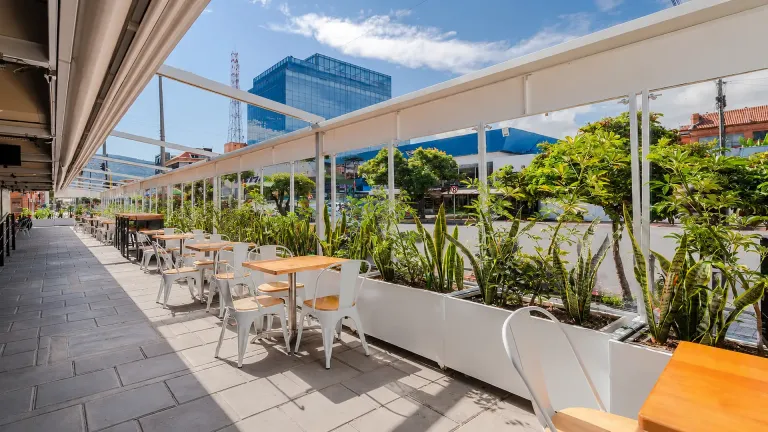 Cerramiento FlexiWind de paneles de vidrio con jardineras integradas, cerrando una terraza de restaurante