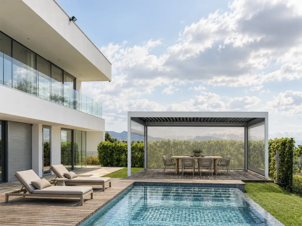 Pérgola cerrada con cortinas FlexiZipp junto a la piscina de una casa, con el comedor exterior bajo la cubierta