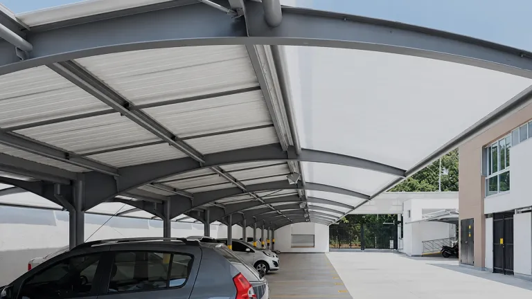 Cubierta para parqueadero de techo curvo translúcido sobre la zona de estacionamiento de un edificio