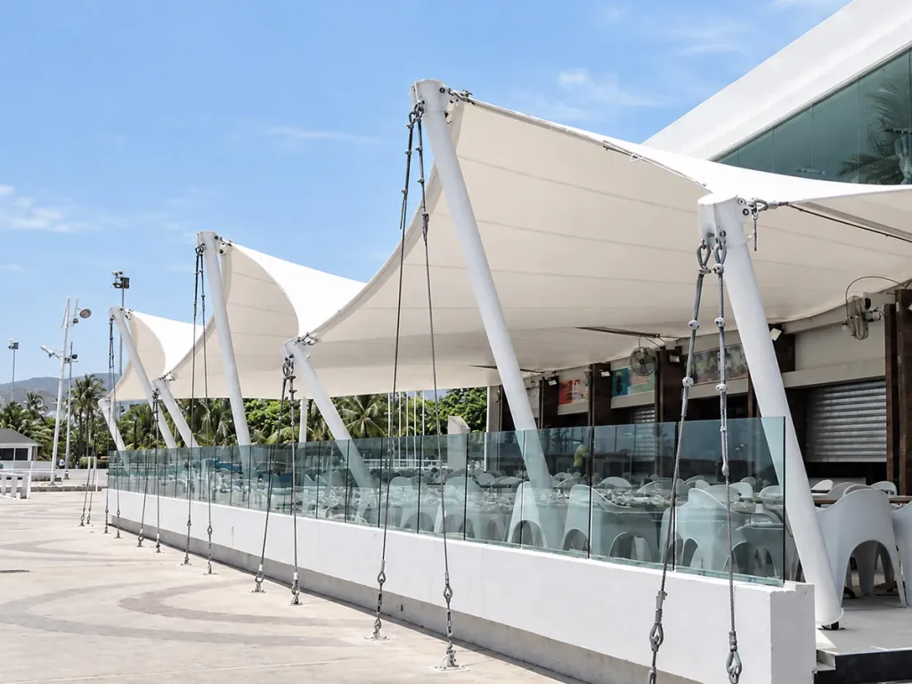 Membranas de pared tensadas con mástiles y cables sobre la terraza de un restaurante con baranda de vidrio