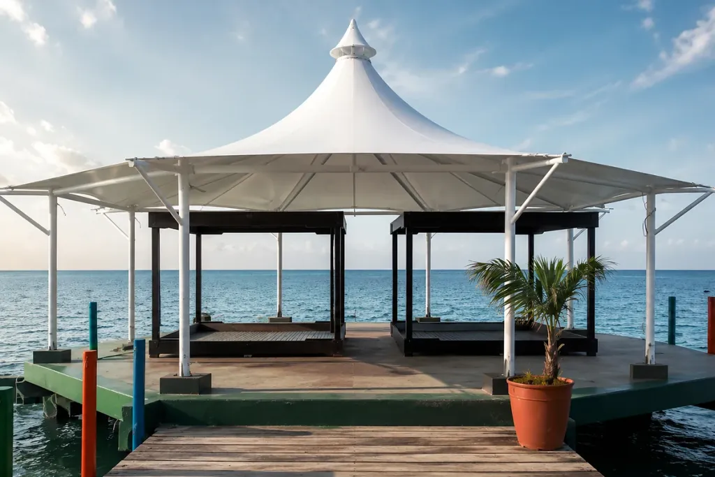 Membrana tipo kiosco sobre un muelle frente al mar, con mástiles perimetrales y cono central