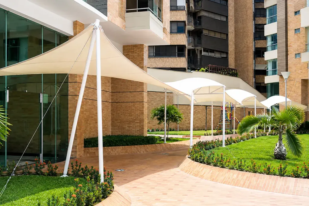 Membranas tipo pañuelo sobre el acceso de un edificio residencial, junto al jardín