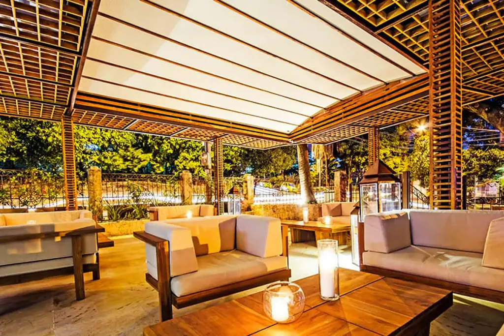 Pérgola fija de acero cubriendo el lobby exterior de un hotel, con mobiliario de exterior debajo