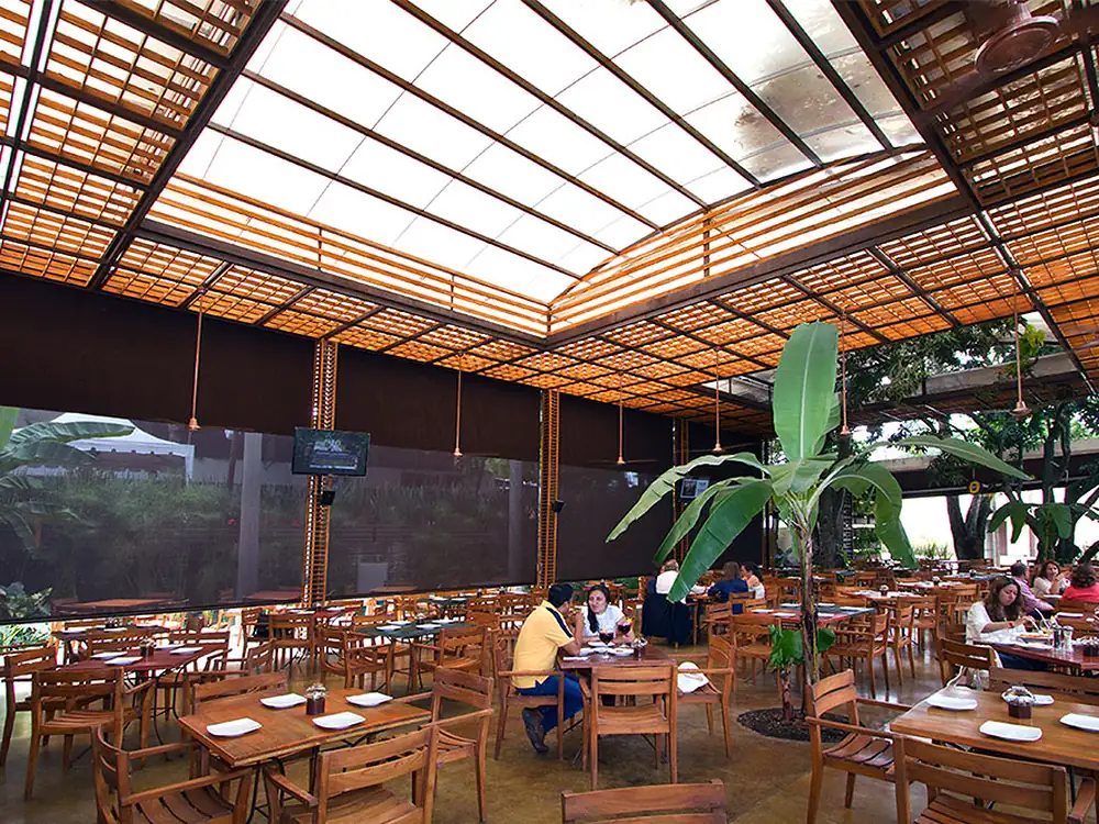 Plazoleta de comidas cubierta con pérgola fija de acero, policarbonato y paneles de madera teca