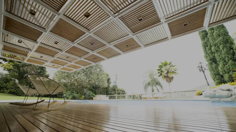 Pérgola fija de aluminio junto a la piscina de una vivienda, con zona de estar cubierta y jardín alrededor