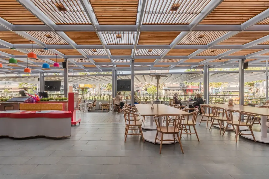 Plazoleta de comidas cubierta con pérgola fija de aluminio y paneles de madera teca