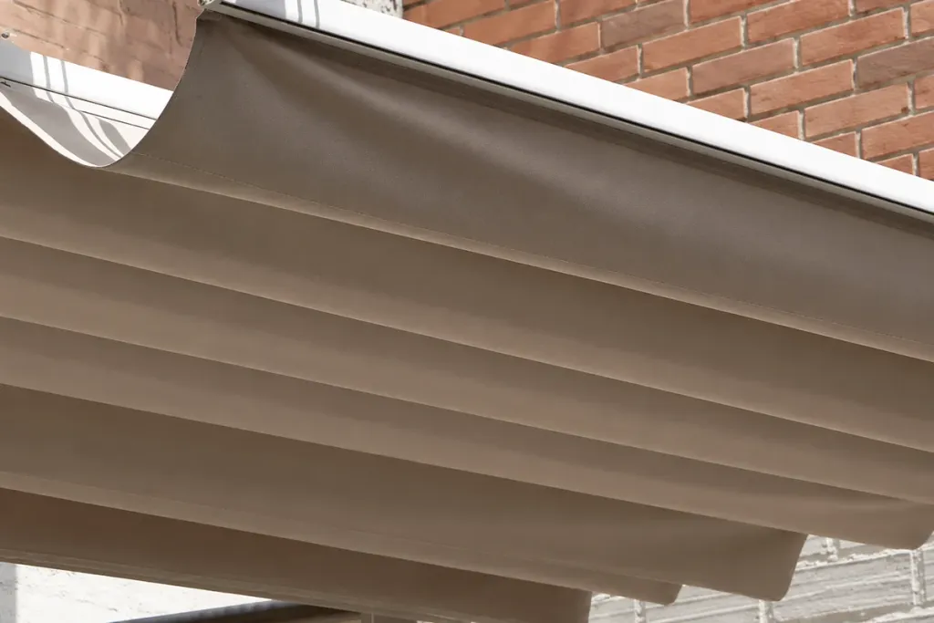Detalle de la lona recogida de la pérgola retráctil contra el muro de ladrillo de Pergamino Café
