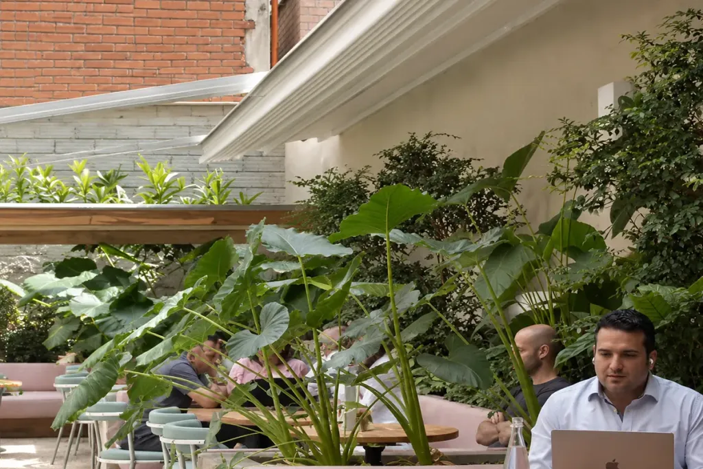 Mesas de Pergamino Café bajo la lona de la pérgola retráctil, con la vegetación de la terraza