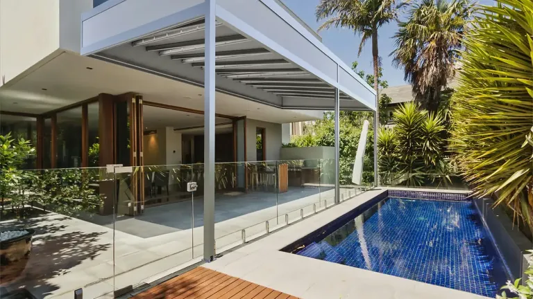 Pérgola retráctil PergoTek Deco con la lona tensada y el marco perimetral de aluminio, sobre la terraza de una casa junto a la piscina