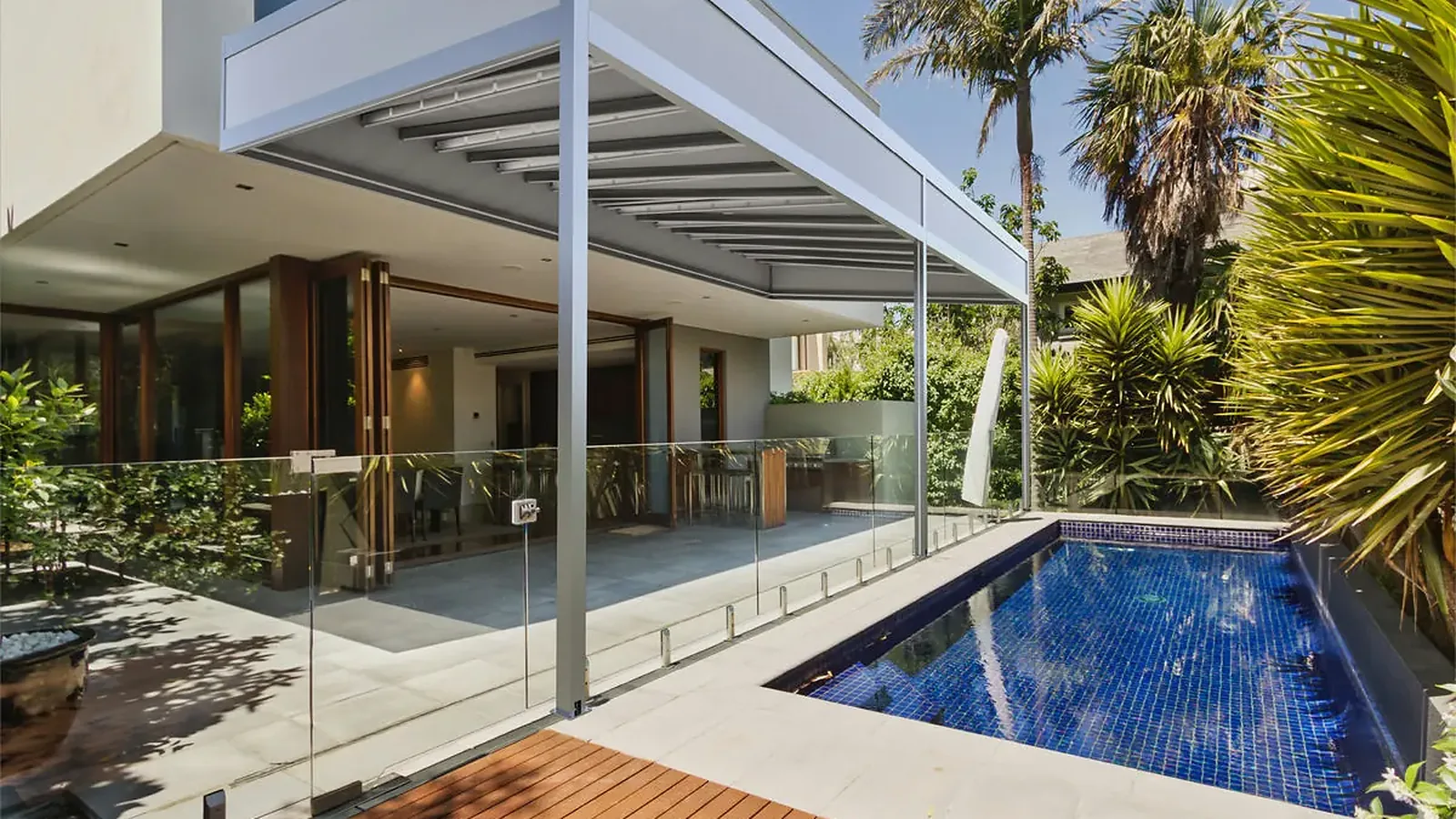 Pérgola retráctil PergoTek Deco con la lona tensada y el marco perimetral de aluminio, sobre la terraza de una casa junto a la piscina