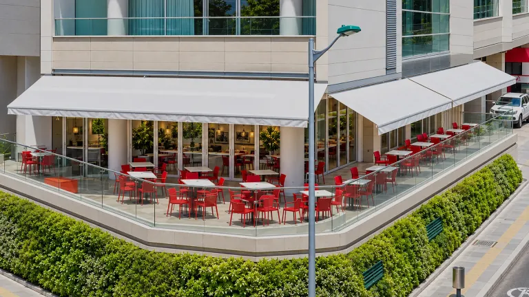 Supersombralinas extendidas sobre la terraza de un restaurante en la esquina de un edificio, con mesas y sillas rojas