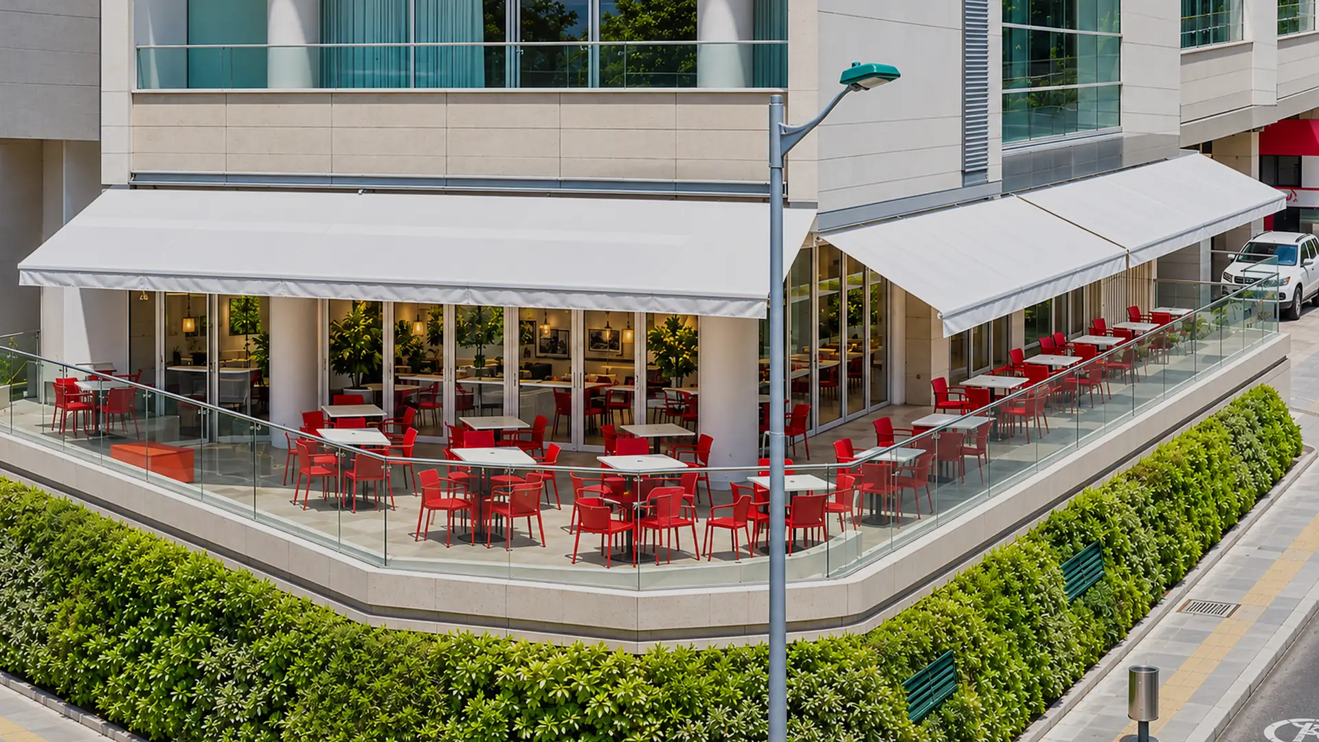 Supersombralinas extendidas sobre la terraza de un restaurante en la esquina de un edificio, con mesas y sillas rojas