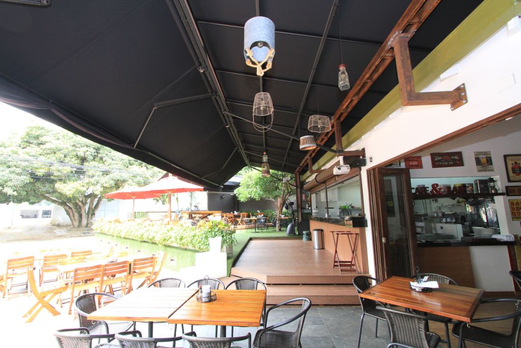 Toldo enrollable de lona negra con faroles sobre la terraza de mesas de un café bar