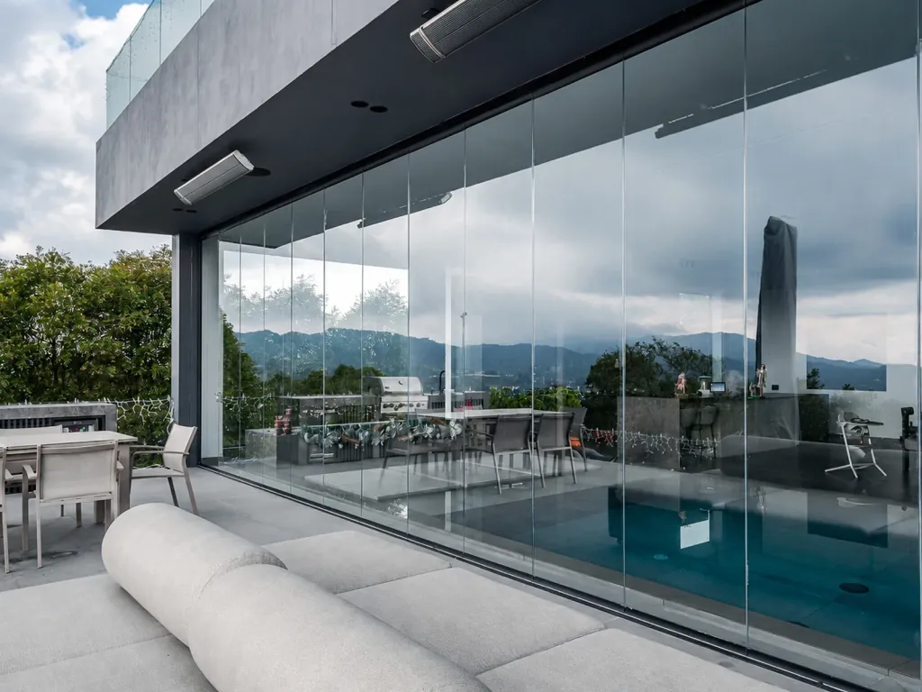 Paneles FlexiGlass de piso a techo que reflejan las montañas, en la terraza de una casa con piscina