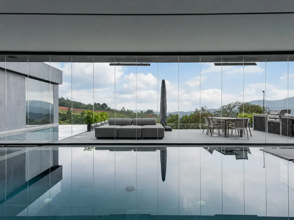 Terraza con piscina vista a través del cerramiento FlexiGlass, con muebles de exterior y montañas al fondo