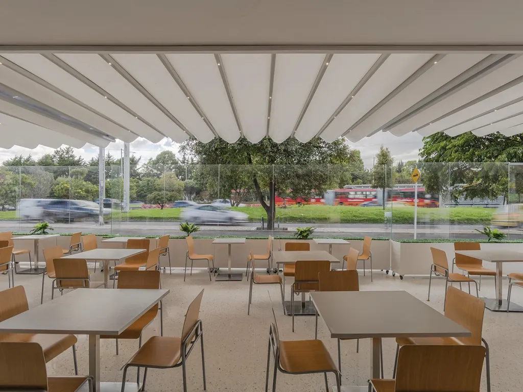 Terraza de restaurante bajo un toldo, con paneles FlexiWind de vidrio en el perímetro frente a la calle