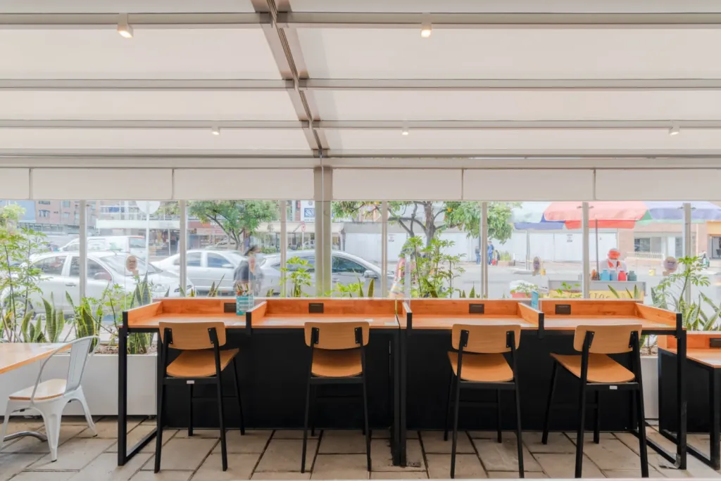 Barra con sillas altas bajo la pérgola retráctil cerrada en la terraza de Carulla Oviedo, Medellín
