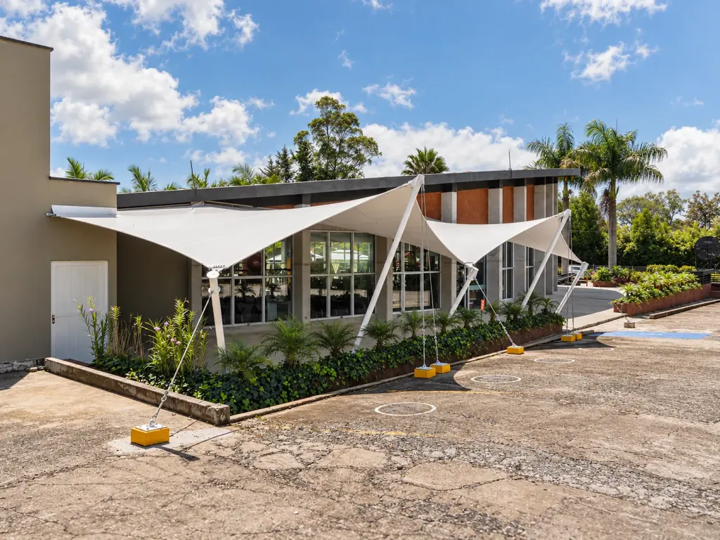 Membranas arquitectónicas tipo pañuelo con mástiles blancos frente a la entrada del Gym Naty Marín
