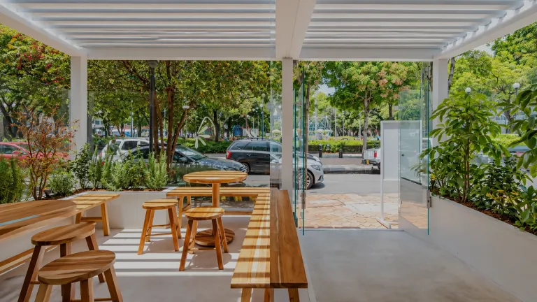 Pérgola bioclimática PergoLam blanca sobre la terraza de un local con mesas de madera
