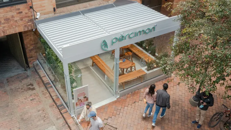 Pérgola bioclimática PergoLam de lamas blancas cubriendo la terraza de Percimon junto a un edificio de ladrillo, vista desde lo alto