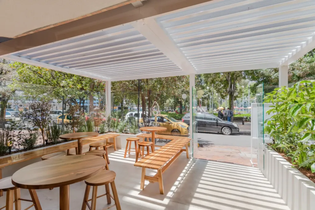 Pérgola bioclimática PergoLam con lamas abiertas sobre la terraza de mesas de Percimon