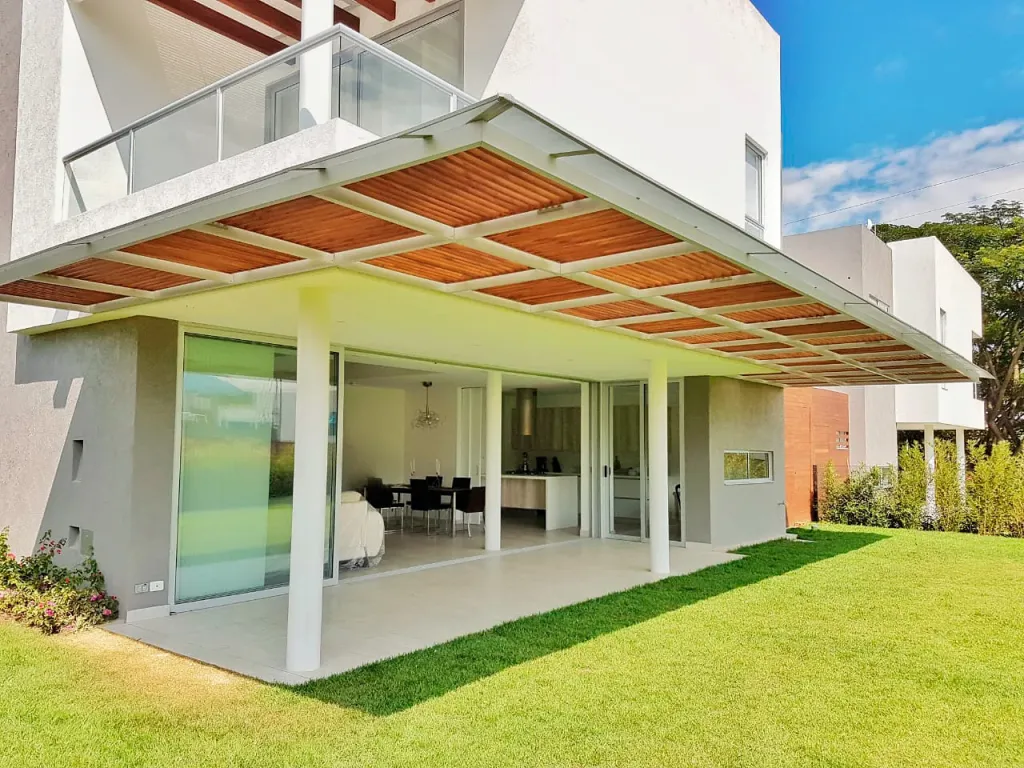 Pérgola fija en aluminio en voladizo sobre la fachada de una casa con jardín
