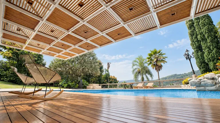 Pérgola fija de madera teca en retícula sobre el deck de una casa campestre frente a la piscina