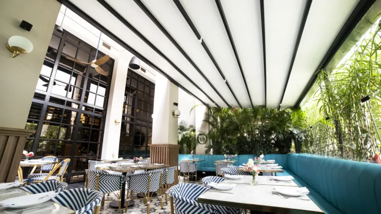 Pérgola retráctil PergoFlex extendida sobre el salón de Odiseo, entre la fachada y la vegetación
