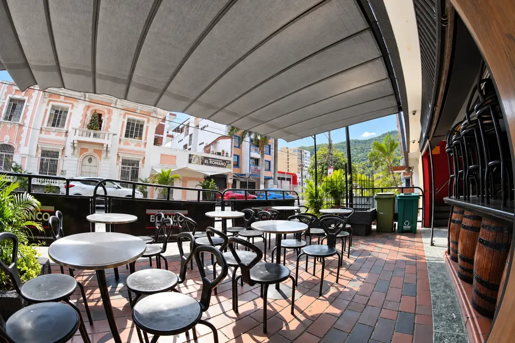 Terraza con piso de ladrillo bajo la pérgola retráctil Pergolite del Viejo Barril, con barriles de madera junto a la fachada