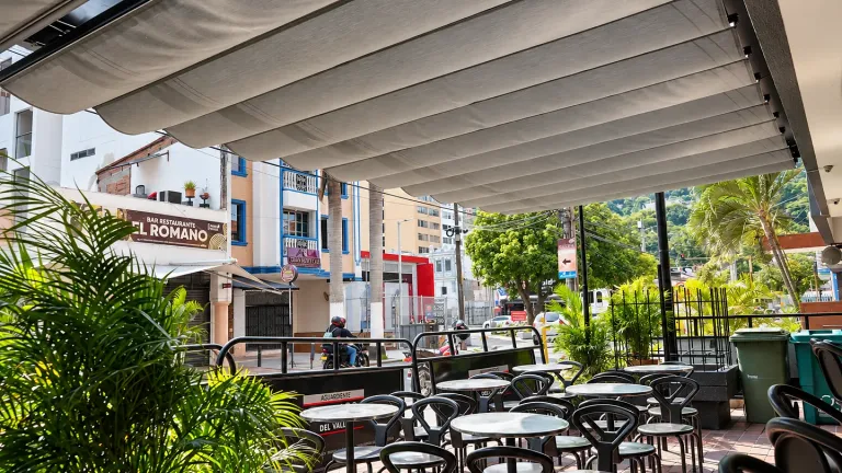 Pérgola retráctil Pergolite de lona gris sobre la terraza de mesas altas del bar Viejo Barril, en una esquina con palmeras