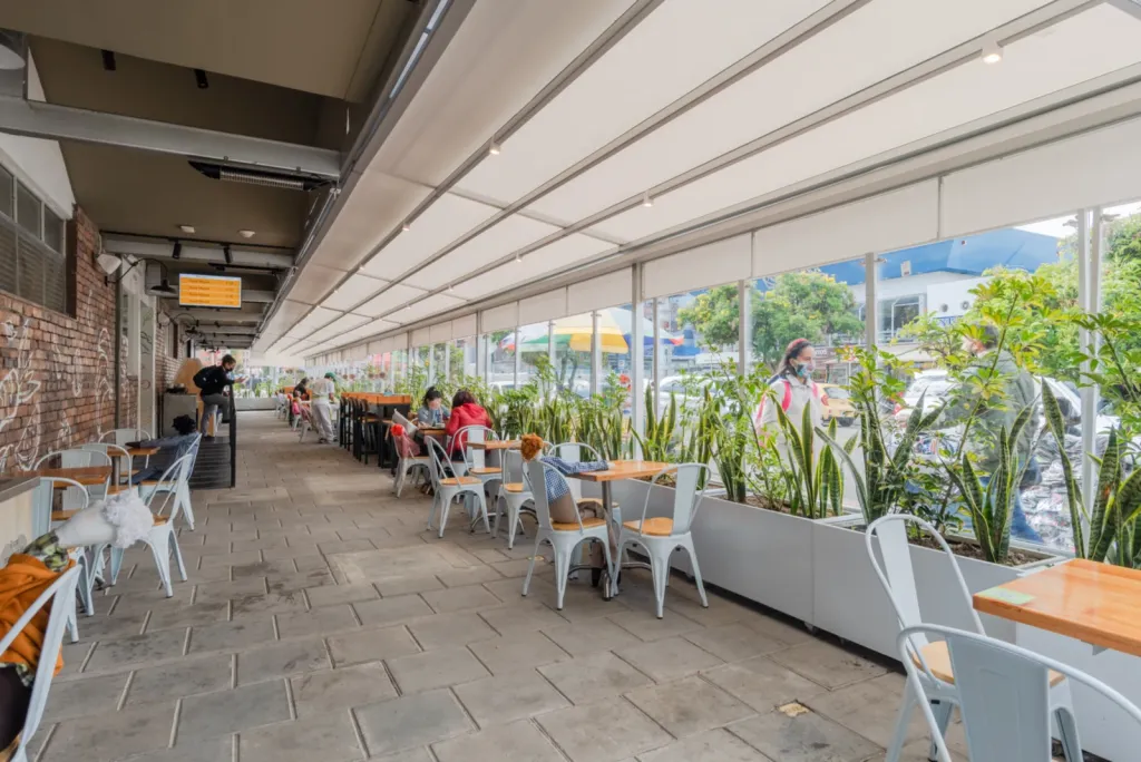 Pérgola retráctil PergoTek sobre la terraza de mesas con jardineras de Carulla Oviedo, Medellín