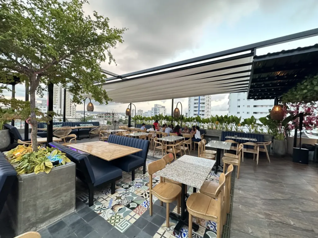 Pérgola PergoTek parcialmente recogida sobre las mesas y bancas tapizadas de la terraza de Ritual