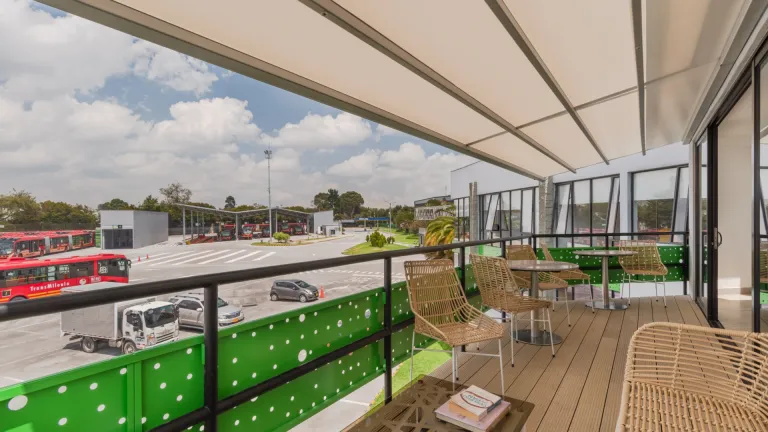 Pérgola retráctil PergoTek cerrada sobre la terraza del Portal 80 de TransMilenio, con los buses al fondo