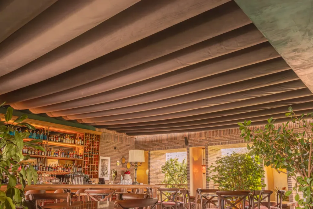 Ondas de lona de la PergoTek vistas desde abajo sobre las mesas de El Zarzo Bar en Medellín