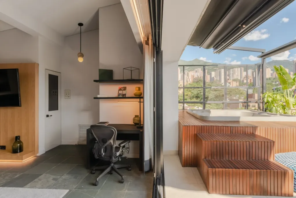 Estudio interior abierto a la terraza del Edificio Atico II con la cubierta retráctil y la ciudad al fondo