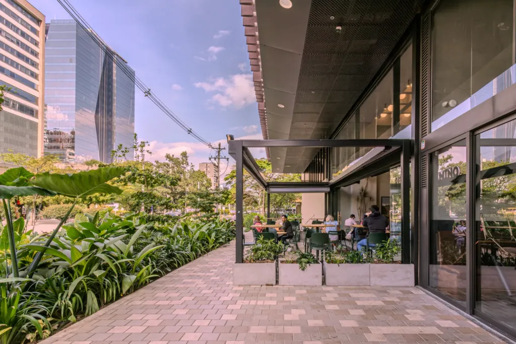 Terraza acristalada con estructura de pérgola de Pergamino Café junto al andén ajardinado en Medellín