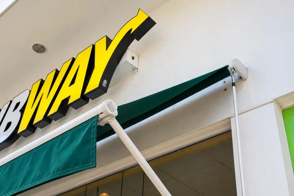 Detalle del brazo proyectante y la lona verde del toldo bajo el letrero de Subway